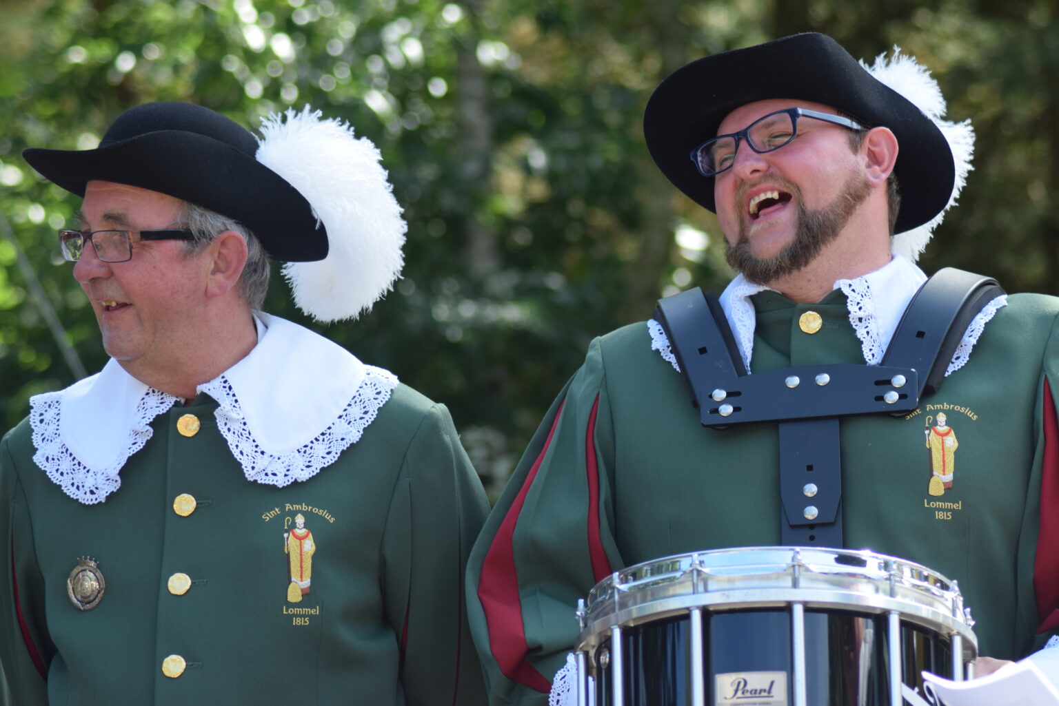 Twee leden van de drumband in groen uniform met hoed en pluim